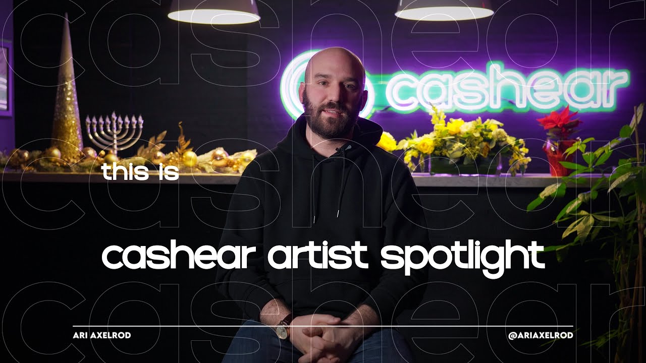 Ari Axelrod in a black hoodie on the Artist Spotlight set, a menorah and gold holiday decor along the counter