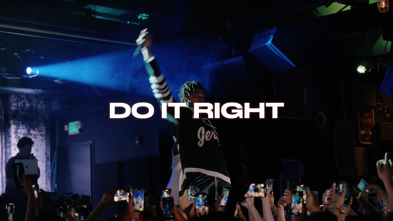 Frame from the Cashear commercial: a performer with a microphone raised above a crowd of phones under blue stage light, DO IT RIGHT across the frame