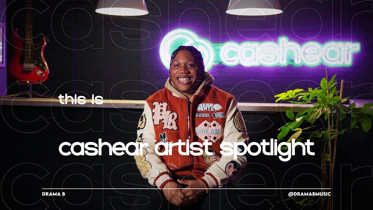Drama B laughing in an orange varsity jacket on the Artist Spotlight set beside the neon cashear sign
