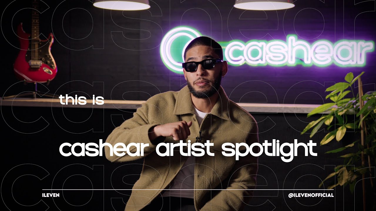 A man in a green racing jersey, cap, and iced chain laughs on the Artist Spotlight set