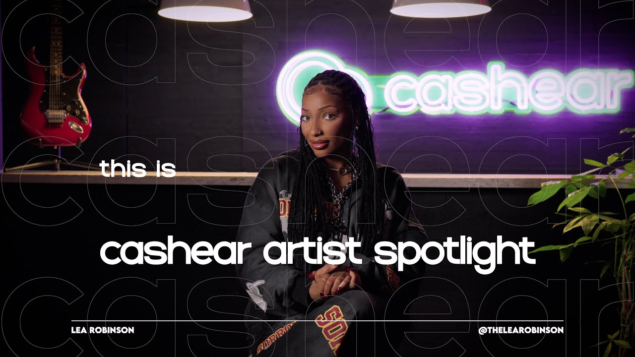 LeA Robinson on the Cashear Artist Spotlight set, braids and a chain necklace, the neon cashear sign and red guitar behind her