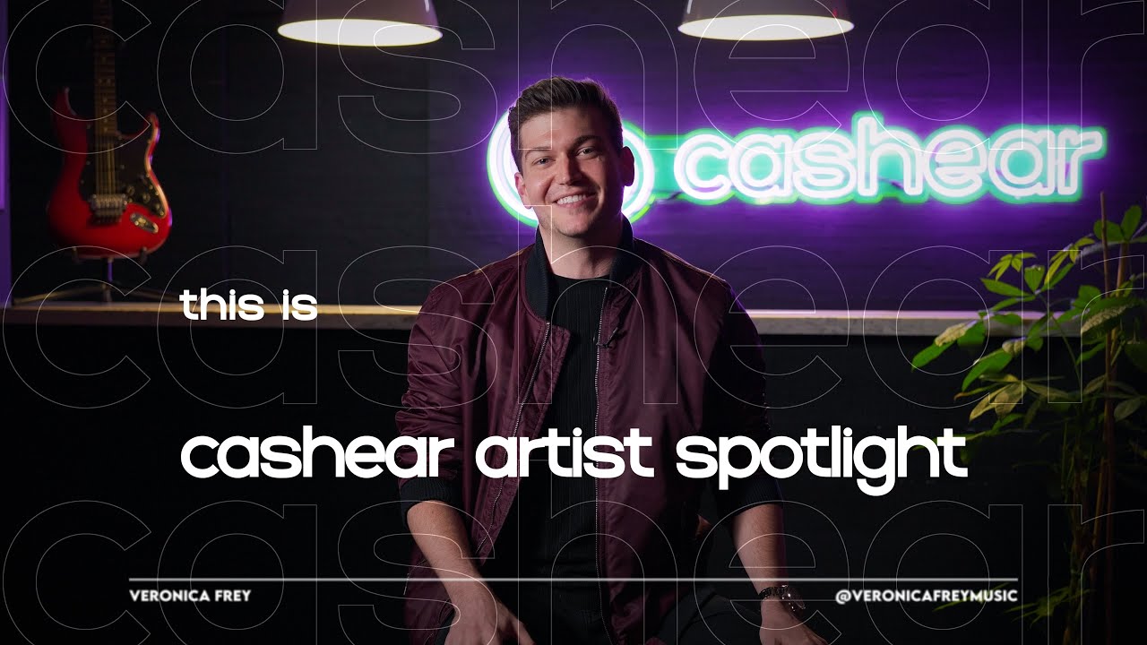 A smiling man in a maroon bomber jacket on the Artist Spotlight set under the neon cashear sign