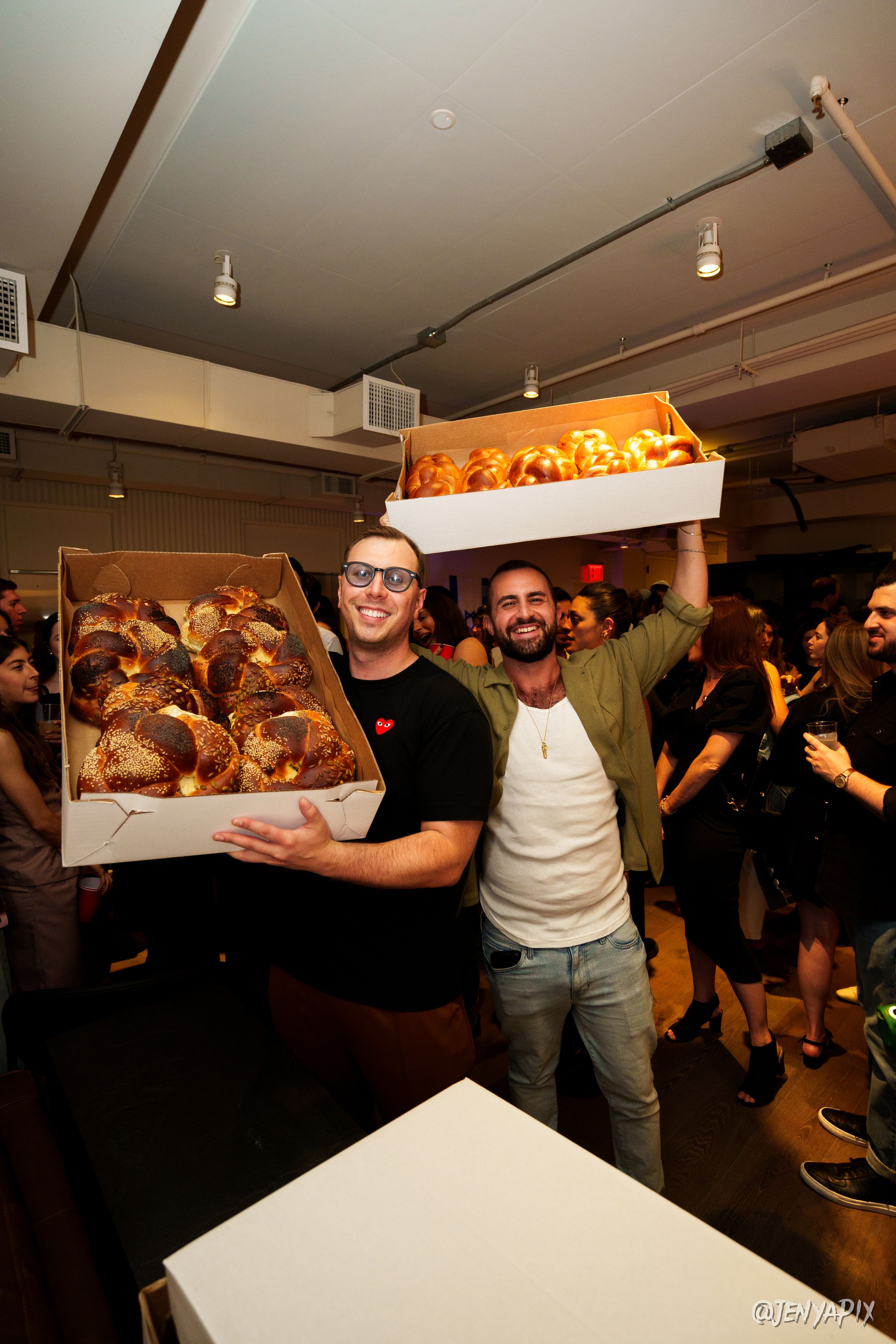 Two guests lifting a wide tray of pastries over a crowded gallery party