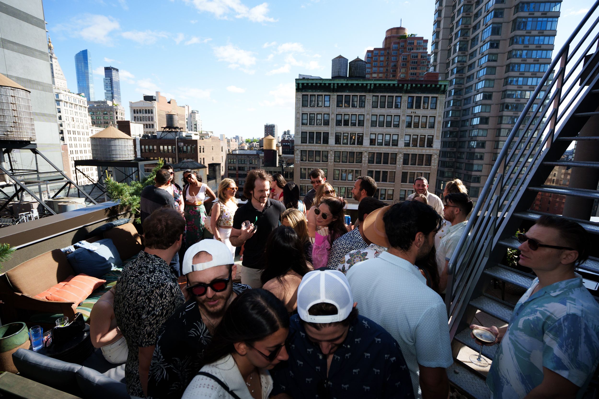 A packed rooftop party in daylight with the Manhattan skyline rising behind the crowd