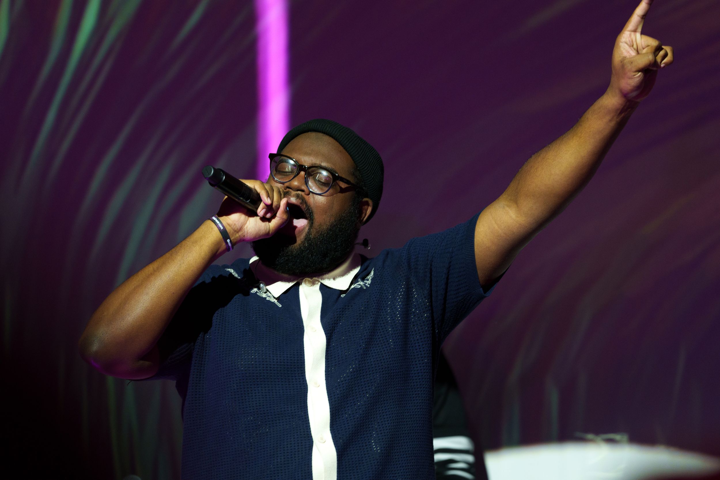 A performer singing into a handheld microphone with one arm raised, purple light streaking behind