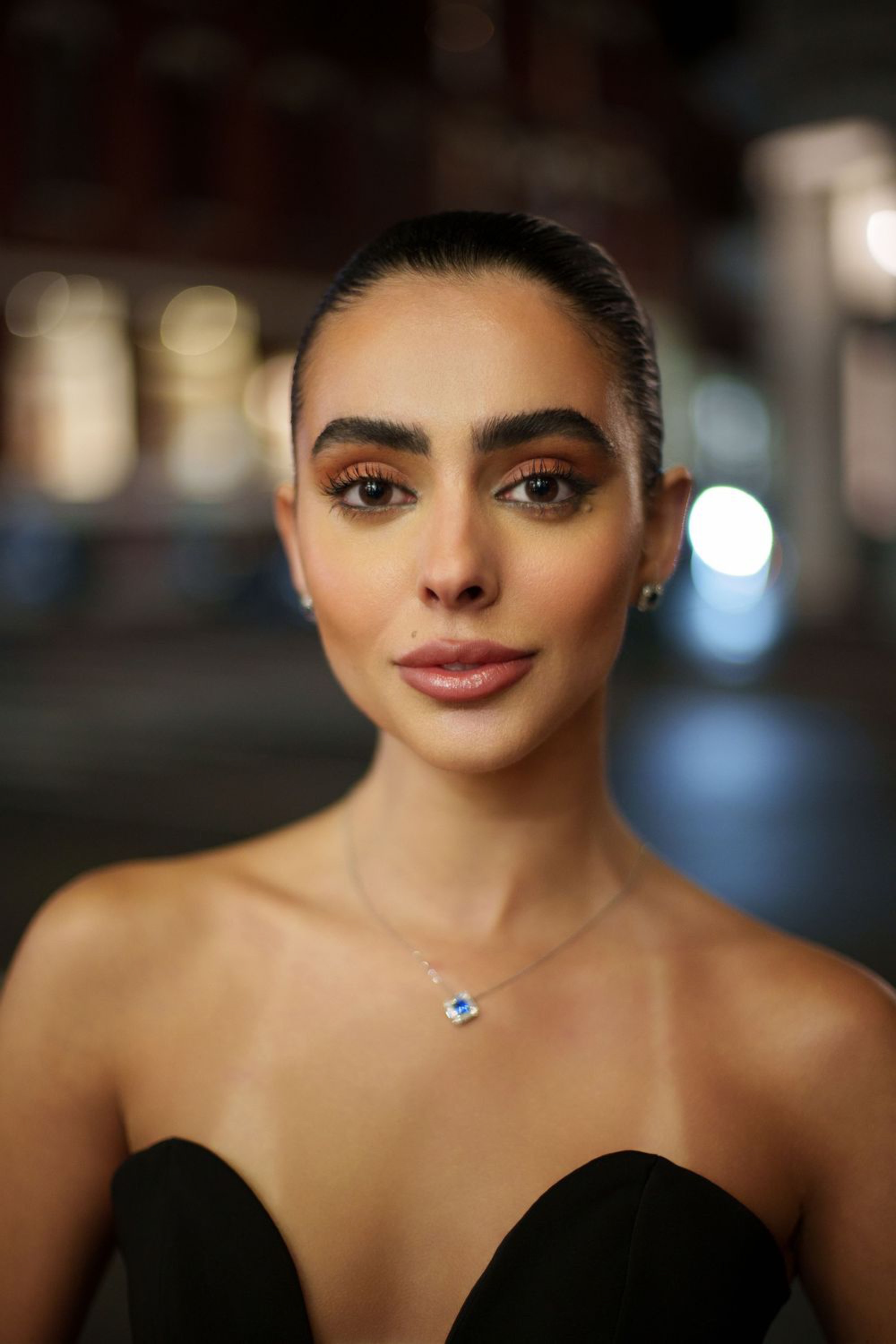 Portrait of a woman in a black strapless dress with slicked back hair and evening makeup at night