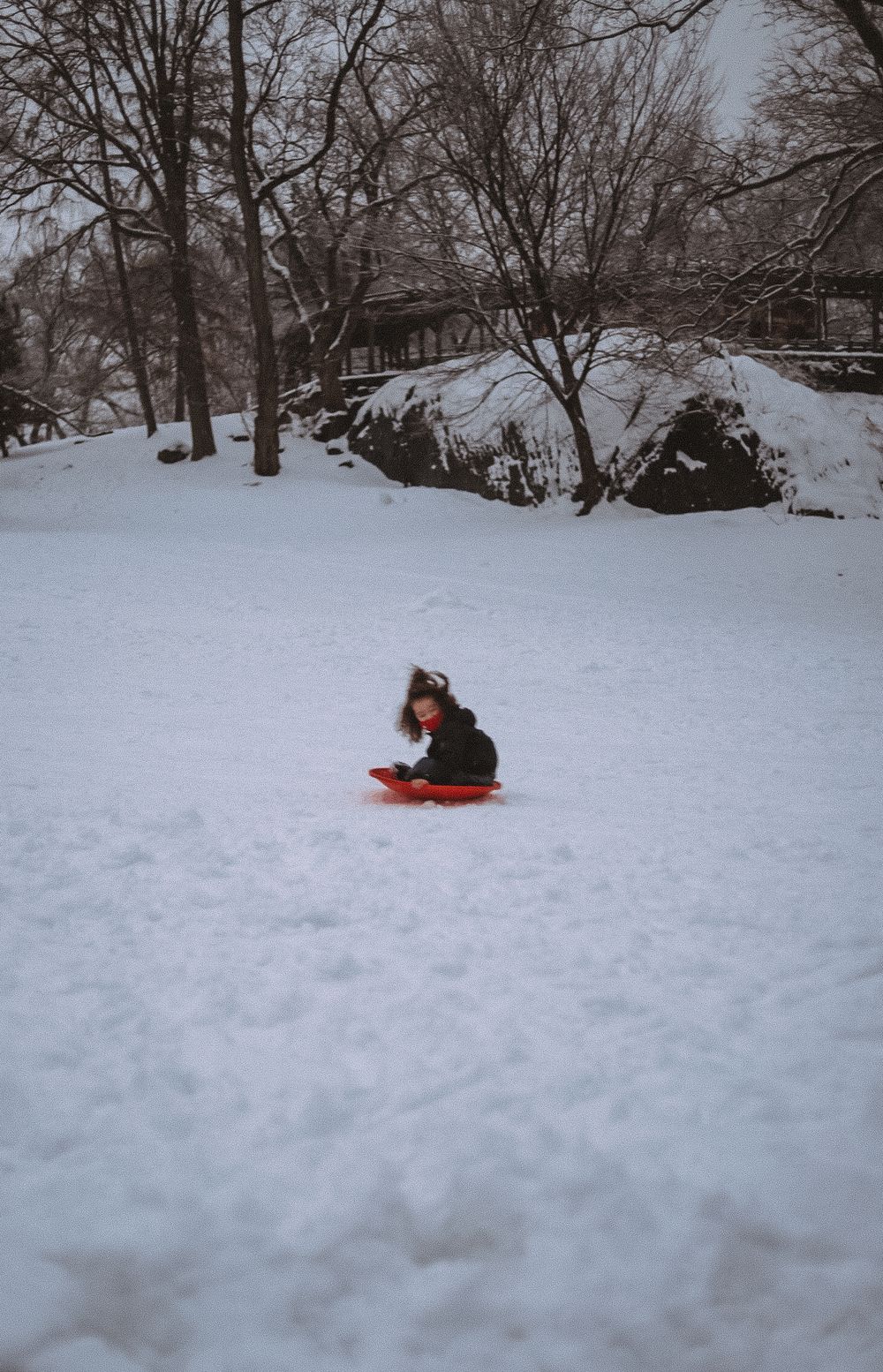 A lone figure sitting in deep snow in an empty winter park under bare trees