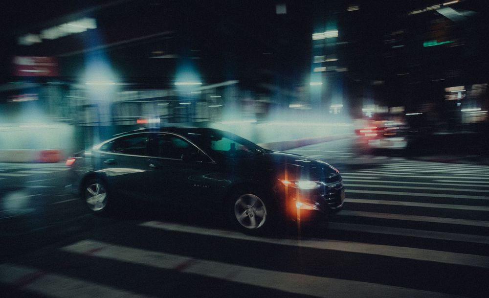 A car crossing a wet intersection at night, the surrounding city lights dragged into streaks