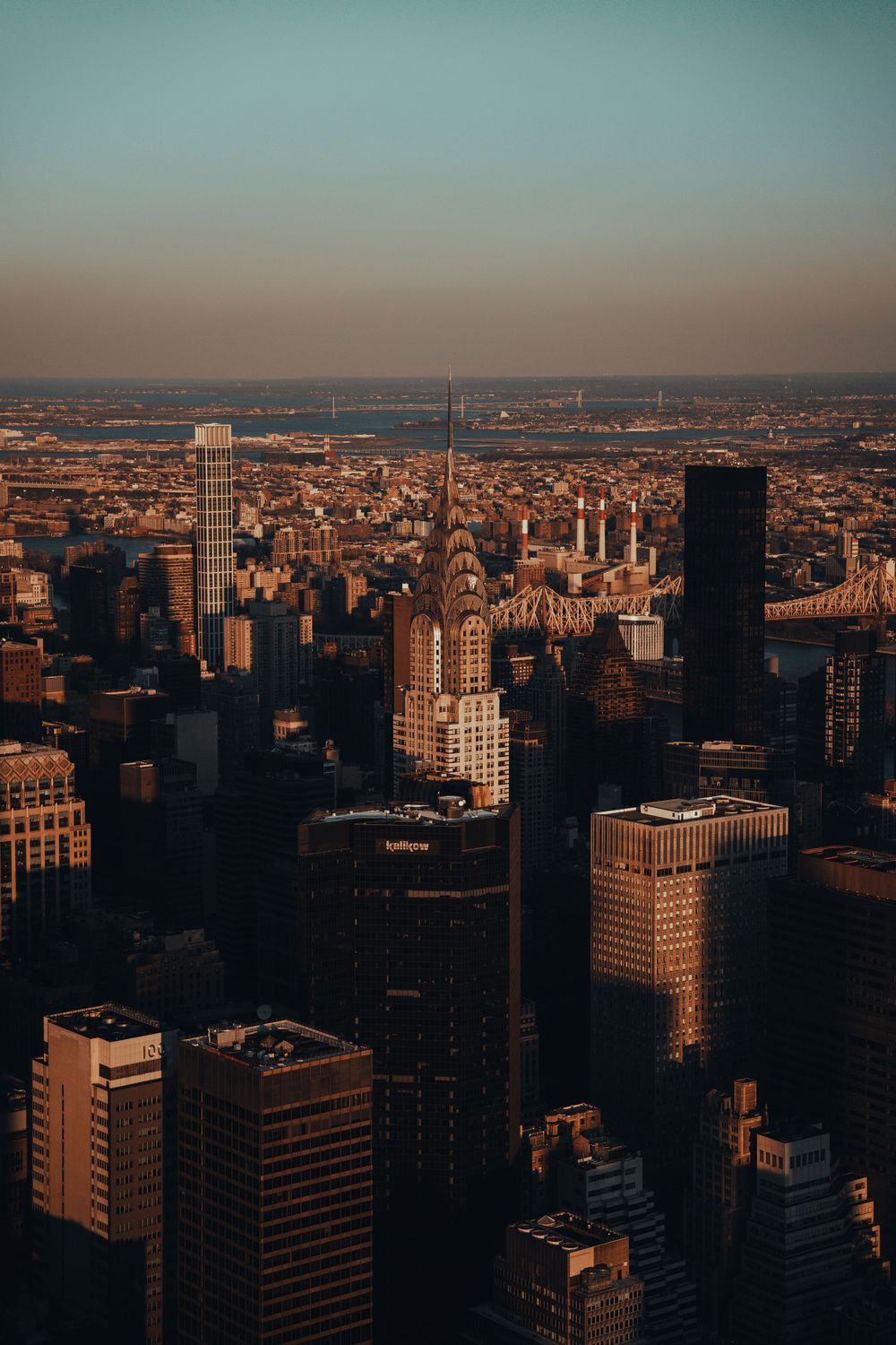 Midtown rooftops and water towers from above at golden hour, the skyline flattening into haze