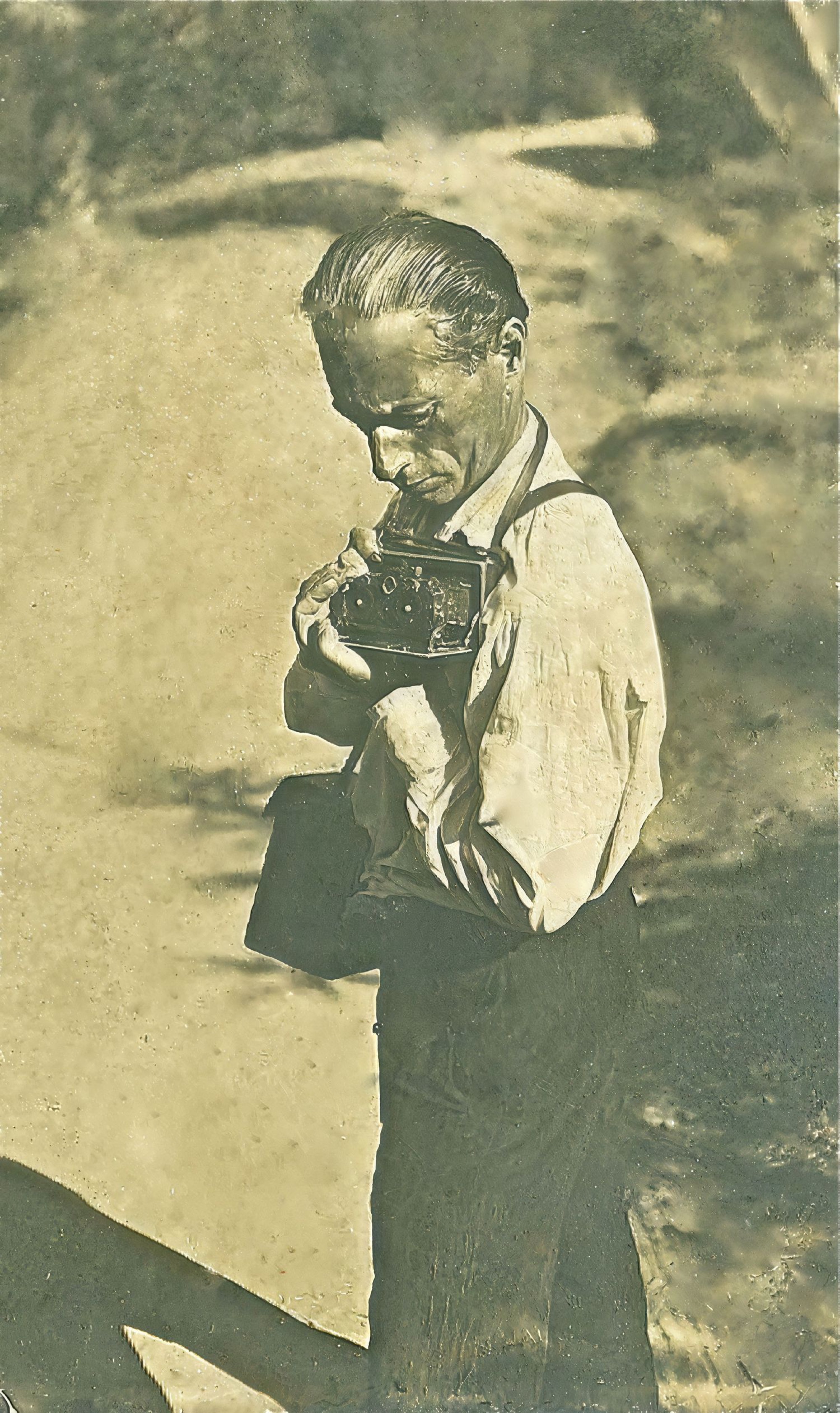 Archival photograph from the Benditskiy family history: a man in period dress and suspenders looking down into a vintage box camera held at chest height