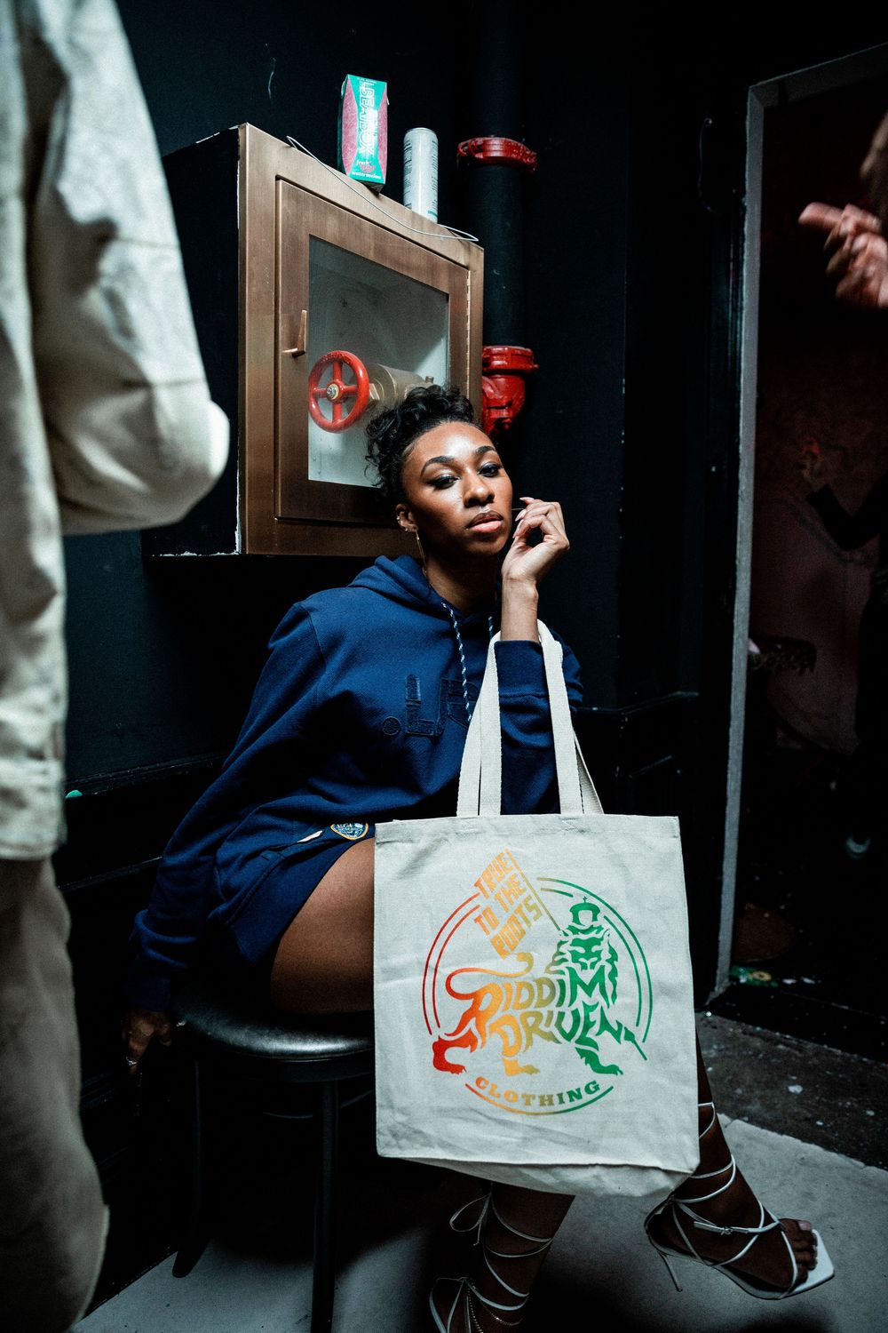 A woman on the phone in a dim doorway, holding a printed canvas tote bag beside a framed picture on the wall