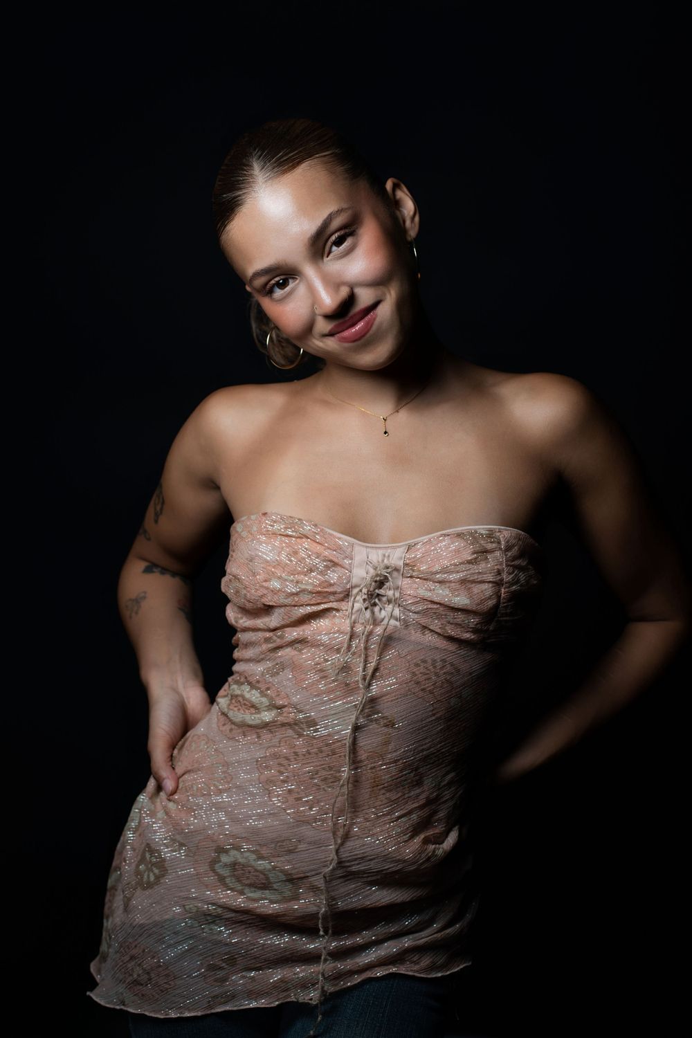 Studio portrait of a woman in a textured strapless dress with one hand on her hip, lit against a black background