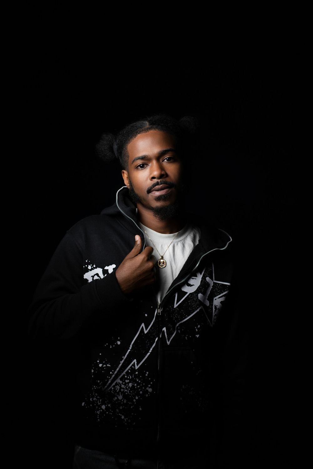 Studio portrait of a man in a black patterned jacket over a white tee, one hand raised to his chest