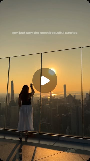 A woman greets the sunrise over the Manhattan skyline from a glass edged observation deck