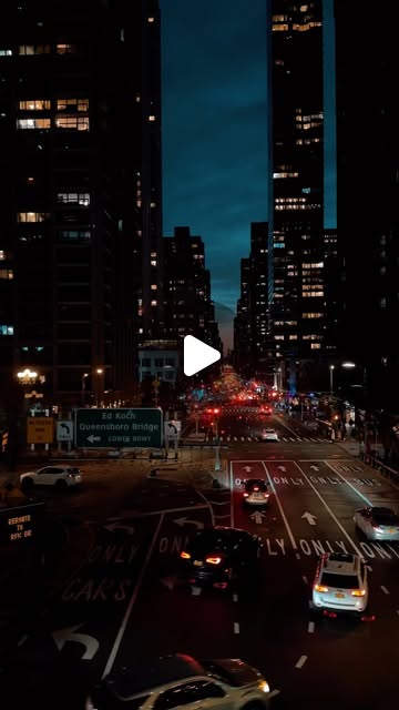Looking down a Manhattan avenue at night, towers lit on both sides and traffic filling the crossing by the Queensboro Bridge signs