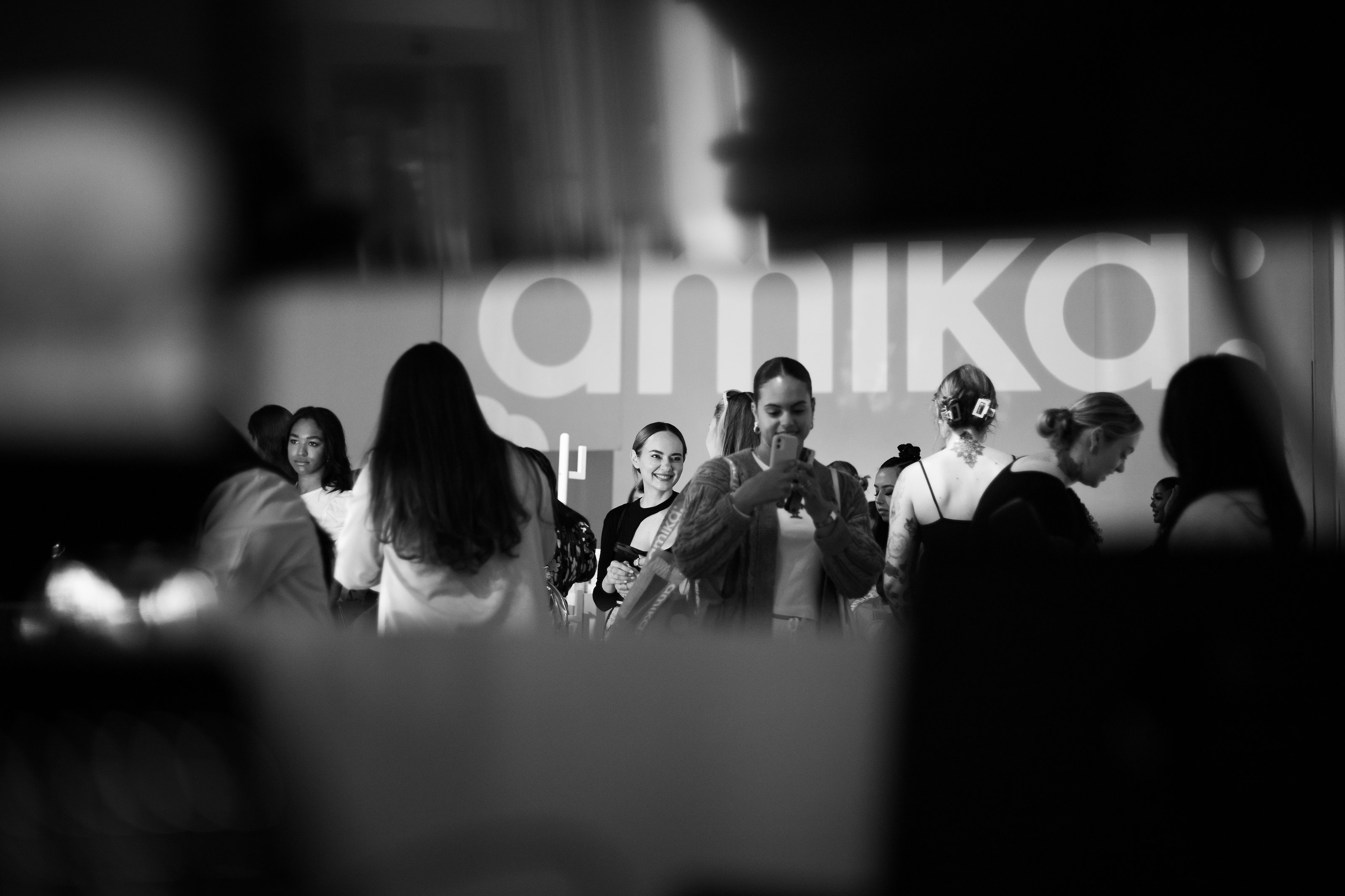 Guests socialize and hold up phones in black and white before a large illuminated Amika wall logo at Lume Studios in Tribeca, Manhattan.