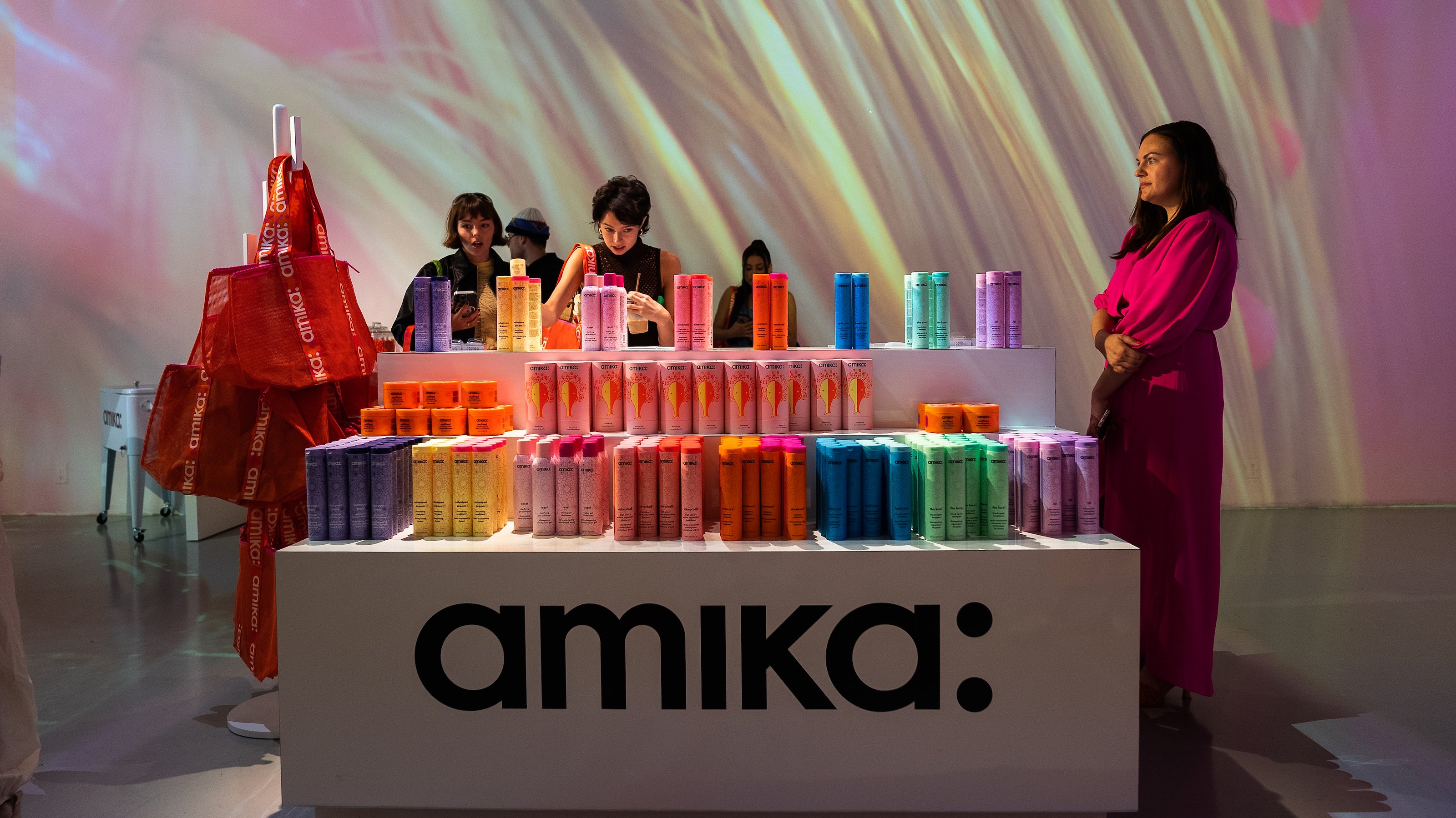 A woman in a magenta dress stands beside a stepped counter showing colorful Amika products at Lume Studios in Tribeca, Manhattan.