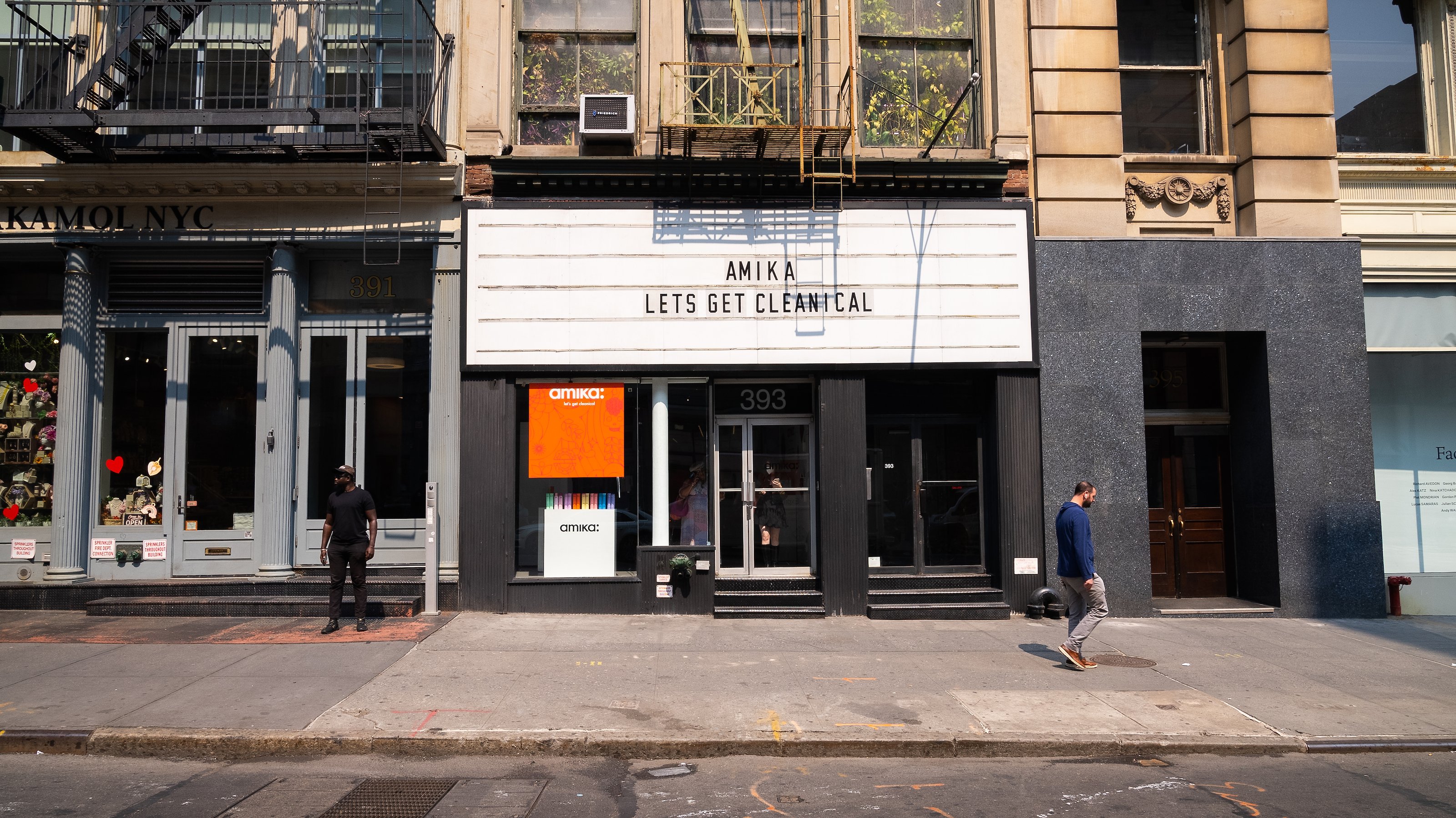 A pedestrian walks past the building facade beneath a white Amika marquee on a sunny sidewalk at Lume Studios in Tribeca, Manhattan.
