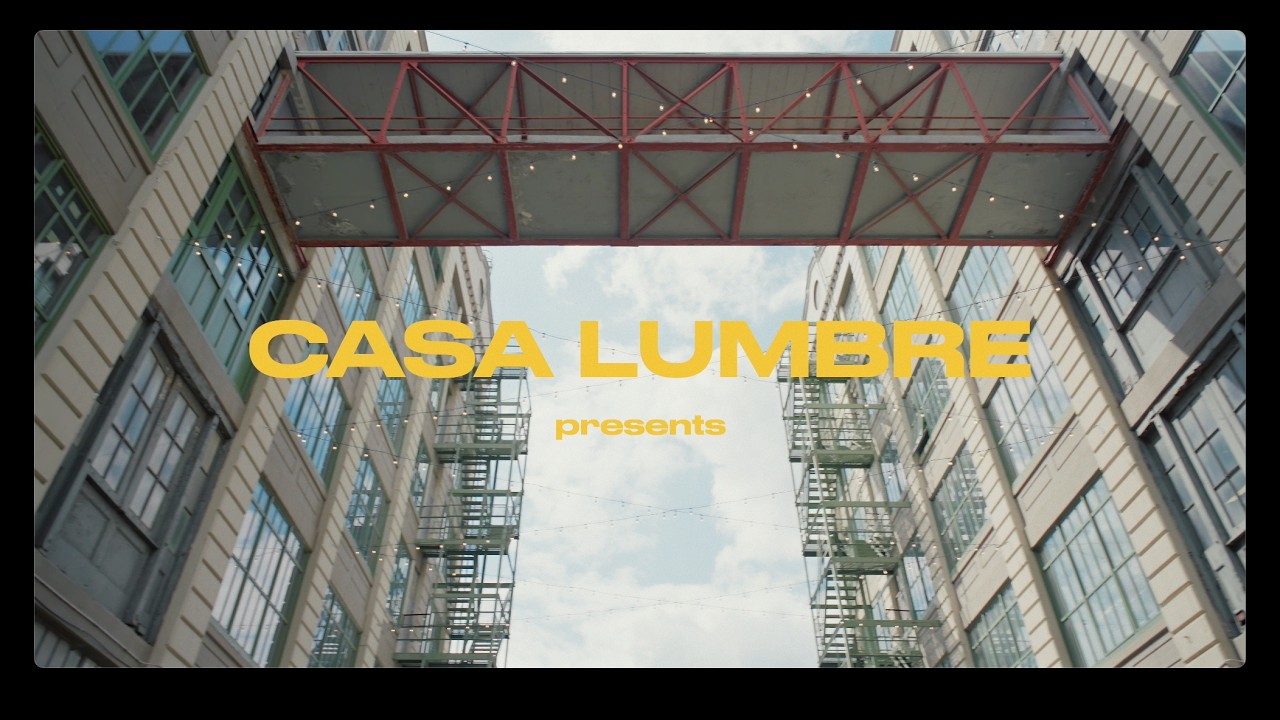 Title frame of the Almave recap film: a Casa Lumbre presents card in yellow type under a red steel bridge connecting two industrial buildings