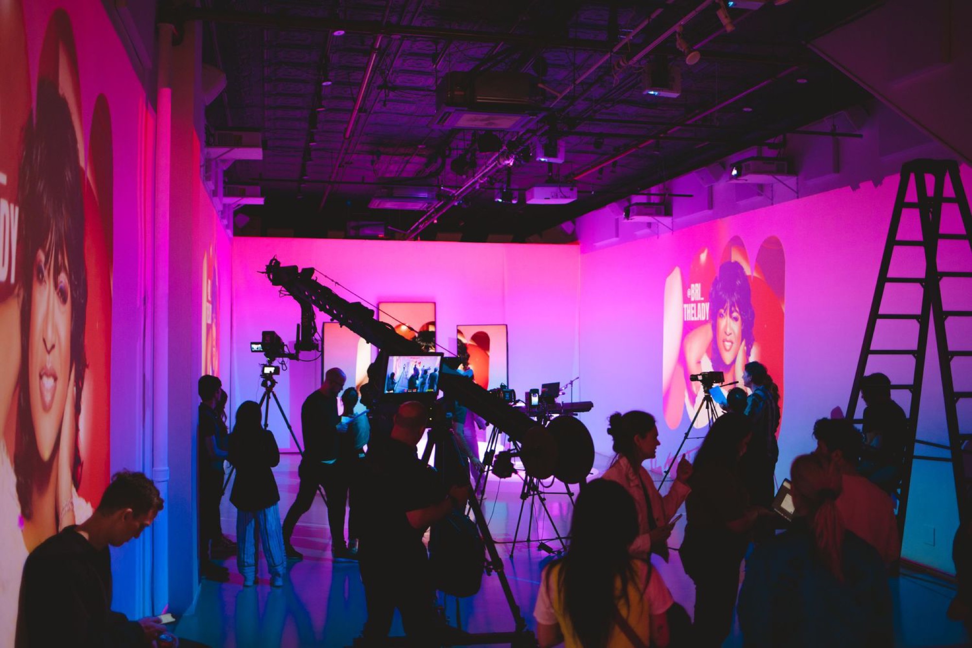 Film crew and audience silhouettes in a studio lit in pink during a live production