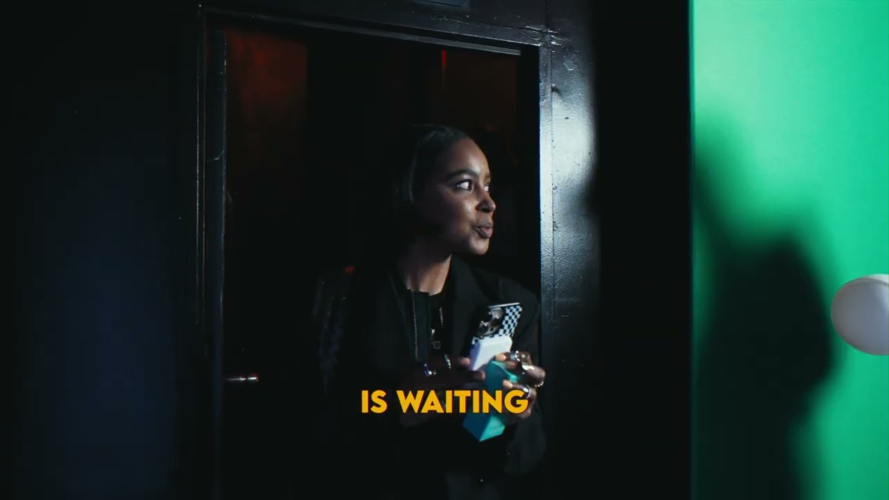 A guest holding a phone and a teal fragrance box looks out from a dark doorway beside a bright green wall