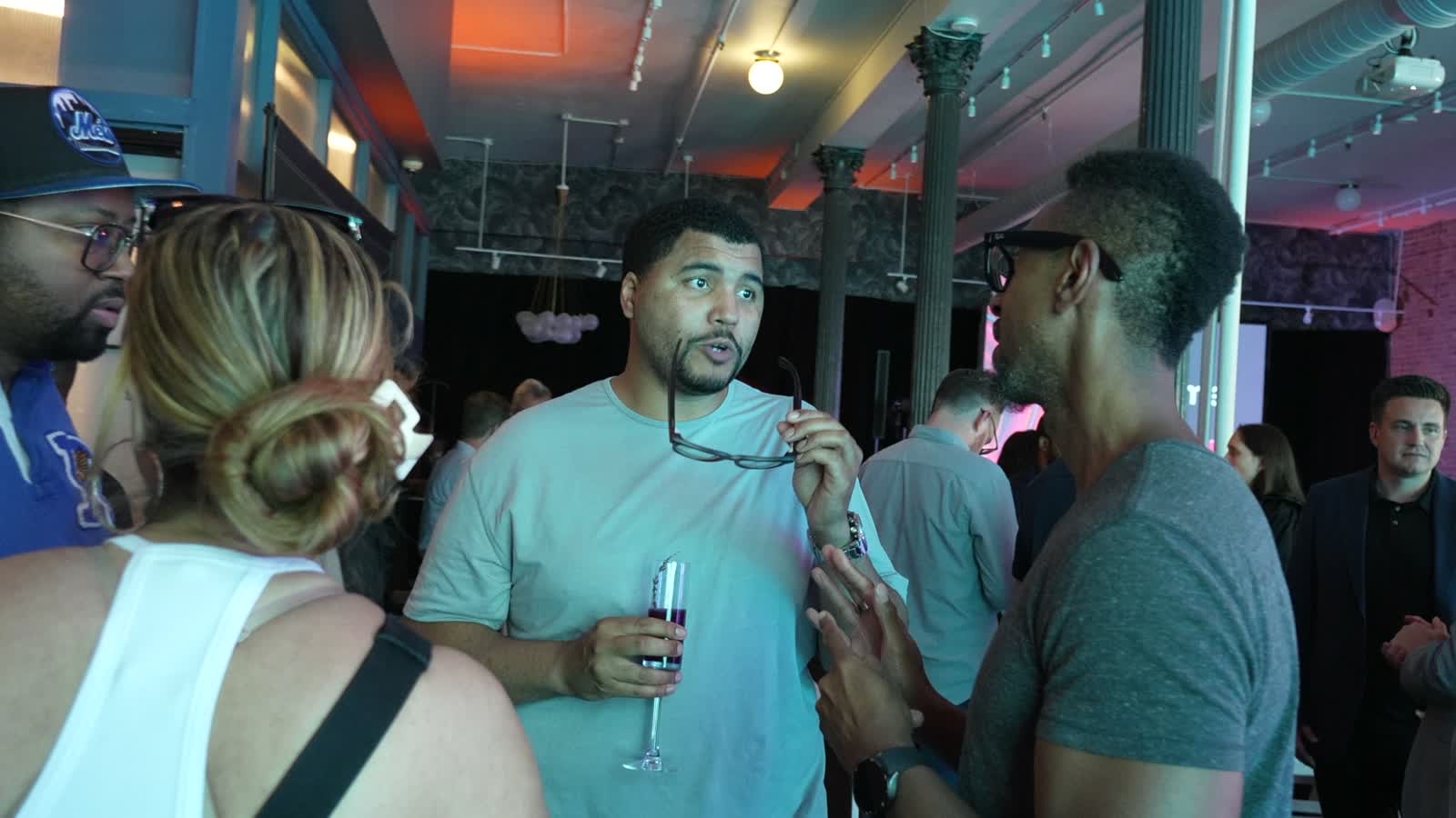 Frame from the TCL keynote film: guests talking with drinks under warm ceiling lights in the room