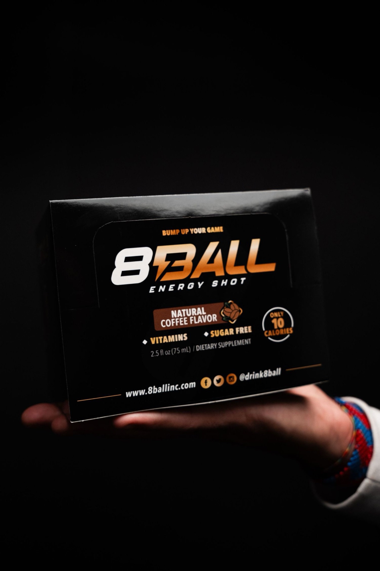 Hand presenting an 8Ball Energy Shot box listing natural coffee flavor, vitamins and only 10 calories