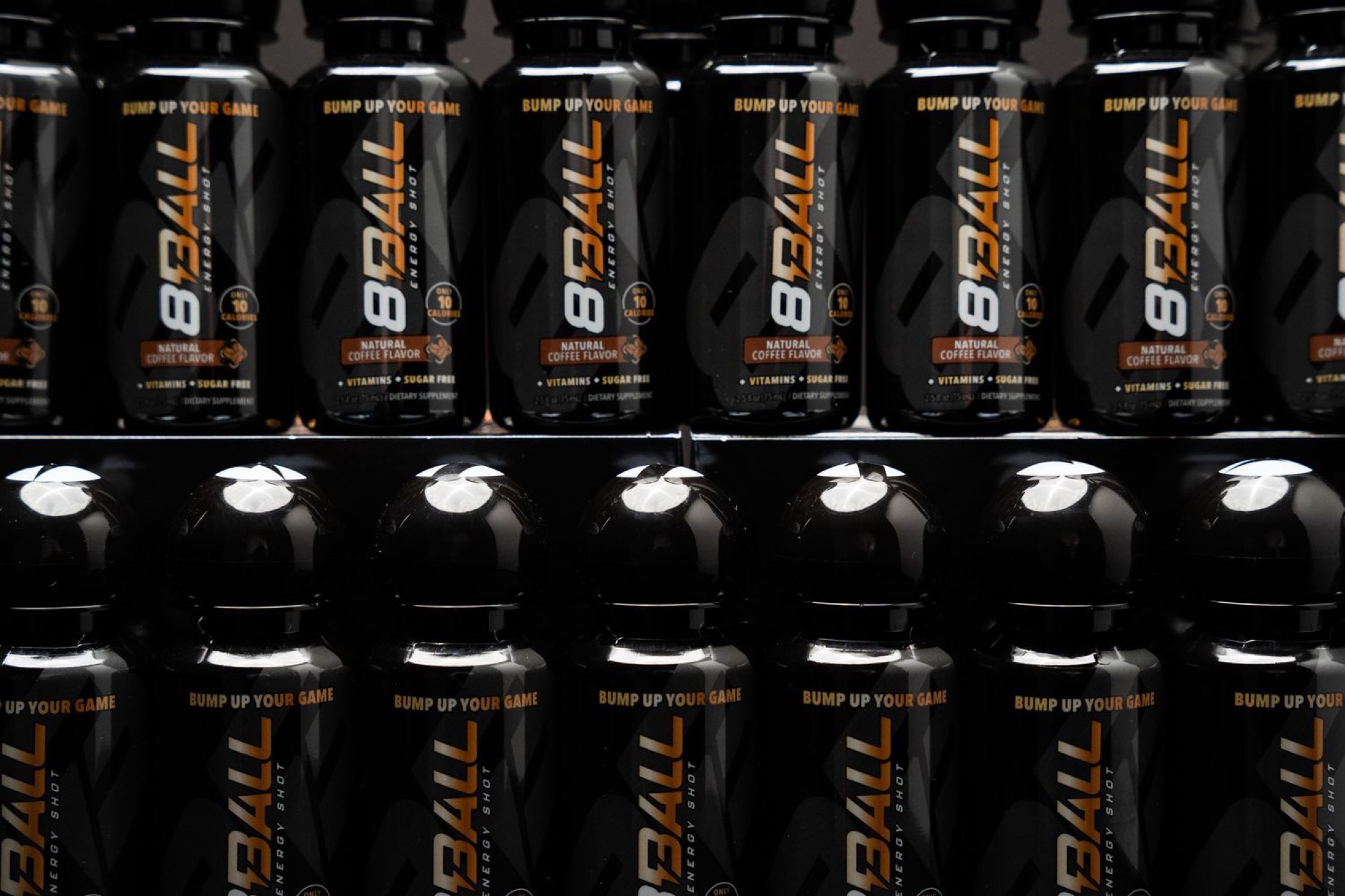 Rows of 8Ball Energy Shot bottles in the coffee flavor lined up across retail shelves, a row of black caps facing the camera between them