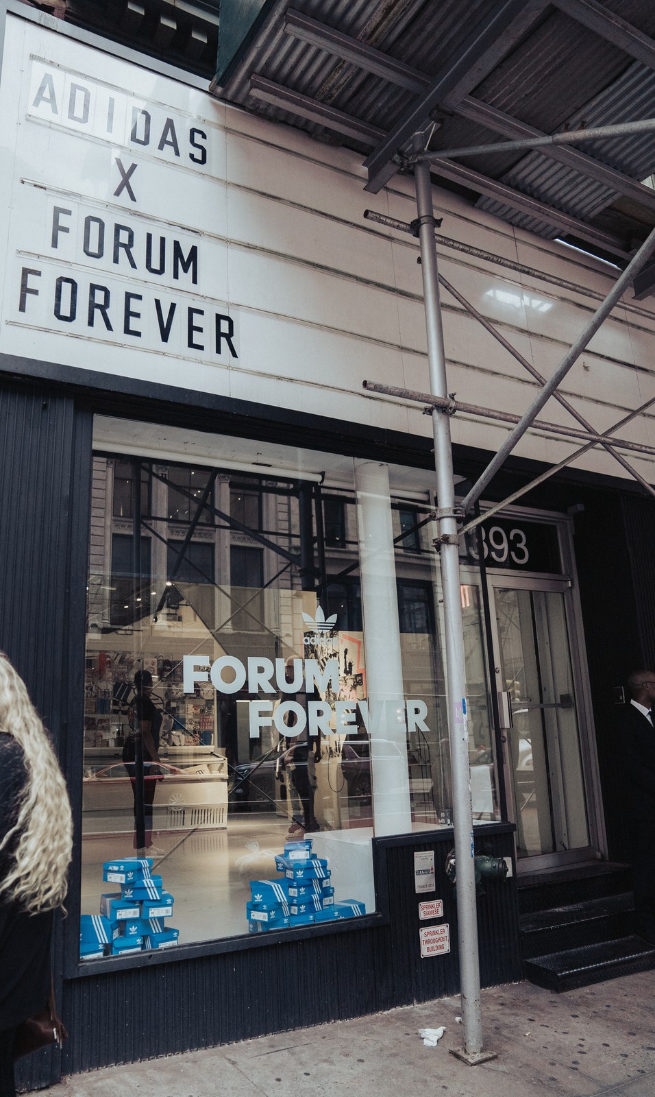 Storefront marquee reading Adidas x Forum Forever above a window display of blue sneaker boxes under scaffolding