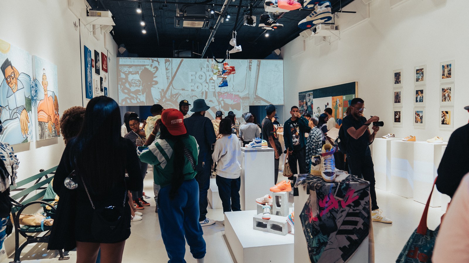 Guests browsing a bright white gallery of sneakers on plinths with a projected mural on the back wall