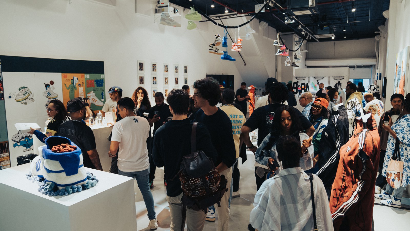 A crowd fills a white gallery with framed art on the walls and a blue sneaker cake on a plinth