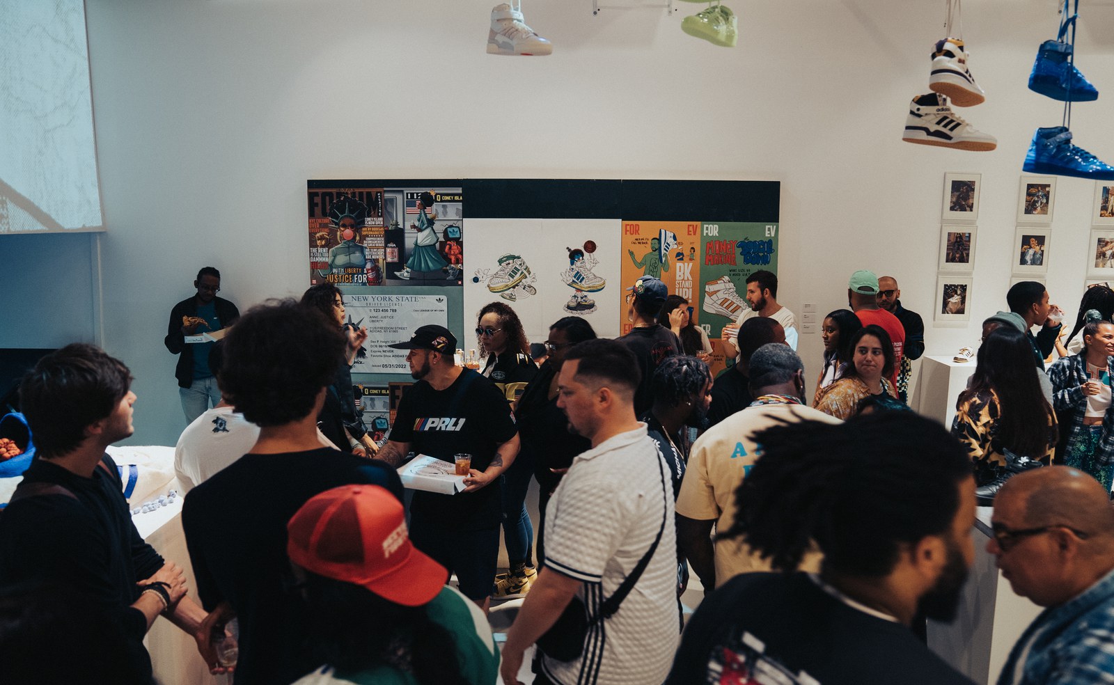 Crowd of guests in caps gathered in a white gallery beneath sneakers hanging from the ceiling
