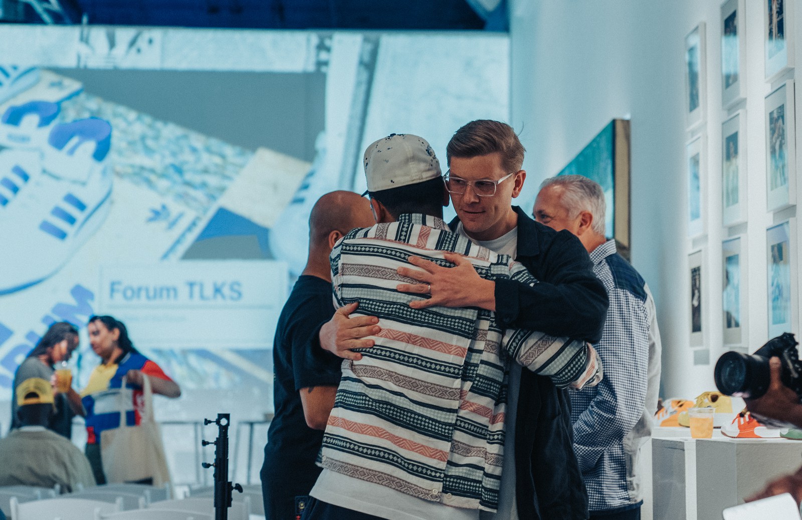 Two men embracing in front of a screen reading Forum TLKS at an Adidas gallery talk