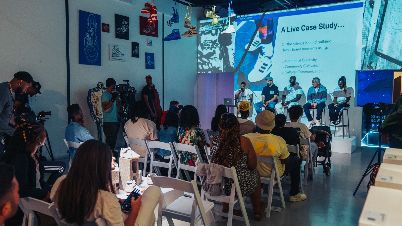 A seated audience watches a panel on stools beside a projected slide reading A Live Case Study
