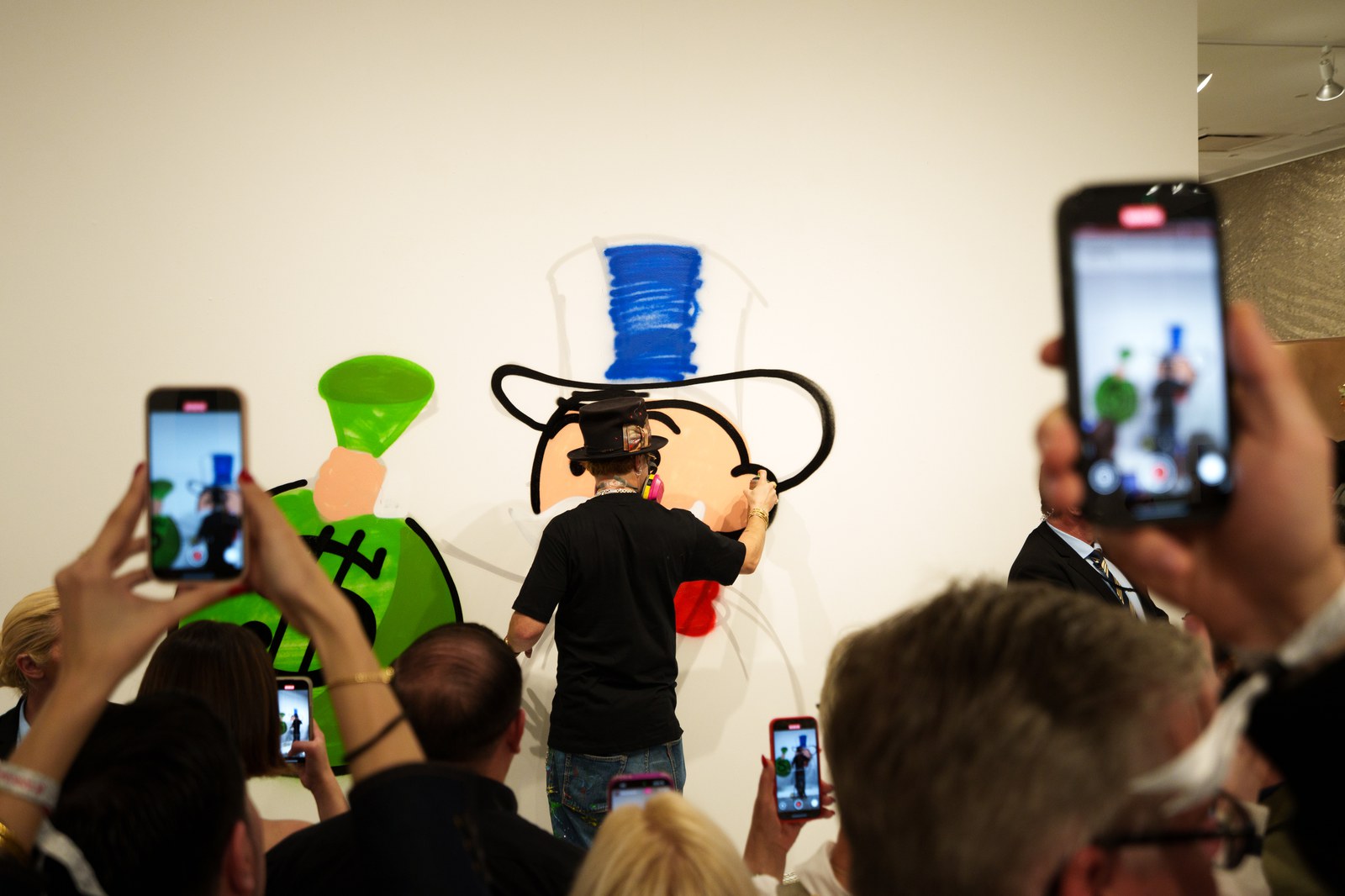 Guests raise phones while the artist outlines a top hat character on the Eden Gallery wall
