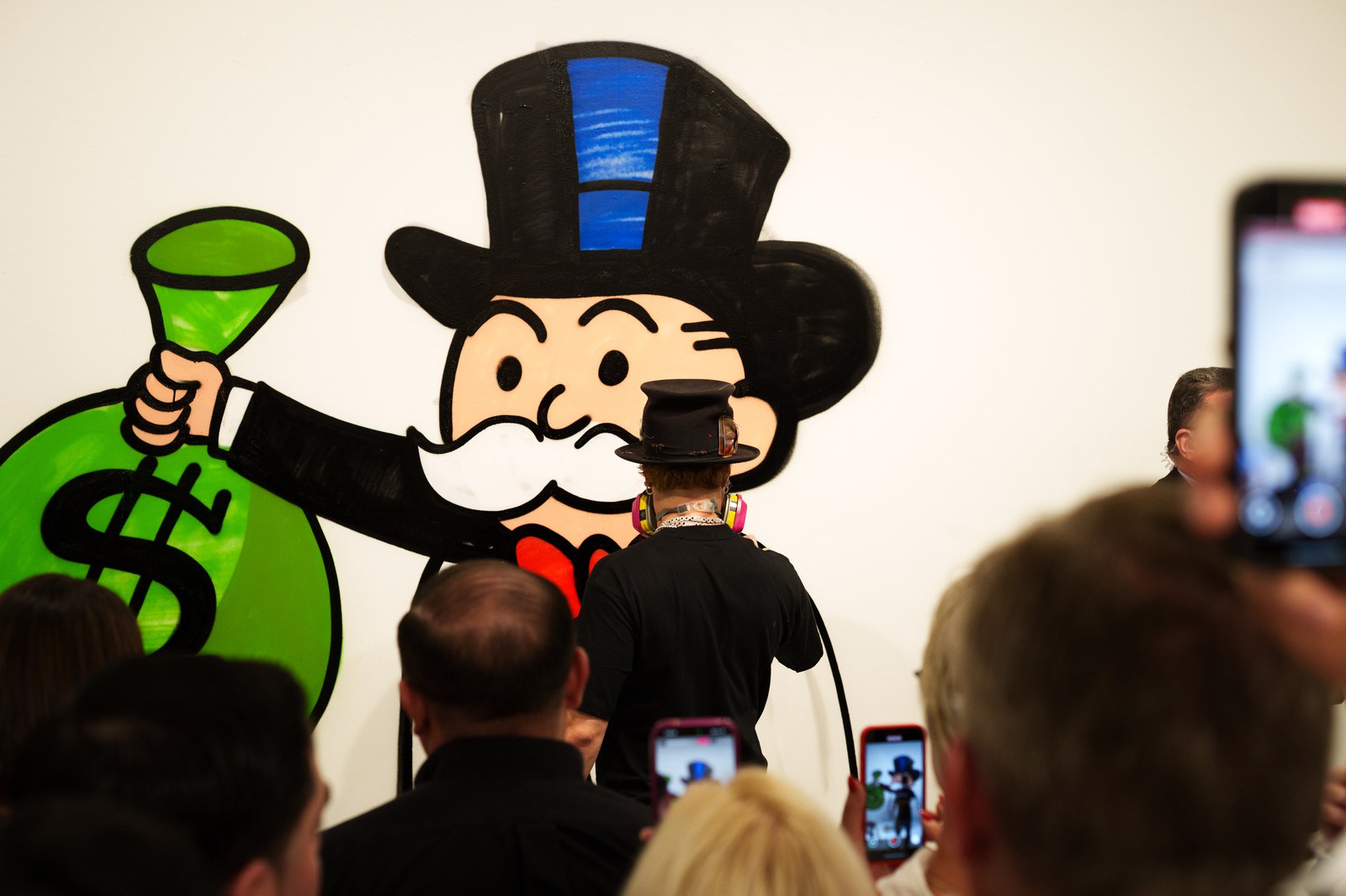 Alec Monopoly spray paints a giant Monopoly Man mural as guests film at Eden Gallery