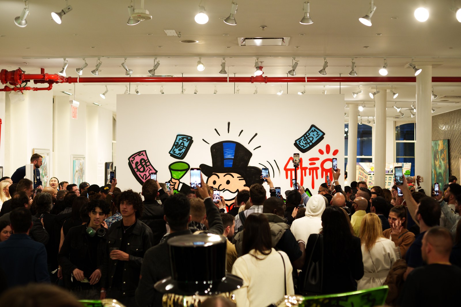 A crowd faces a large mural of a top hatted cartoon figure holding a green drink and cash