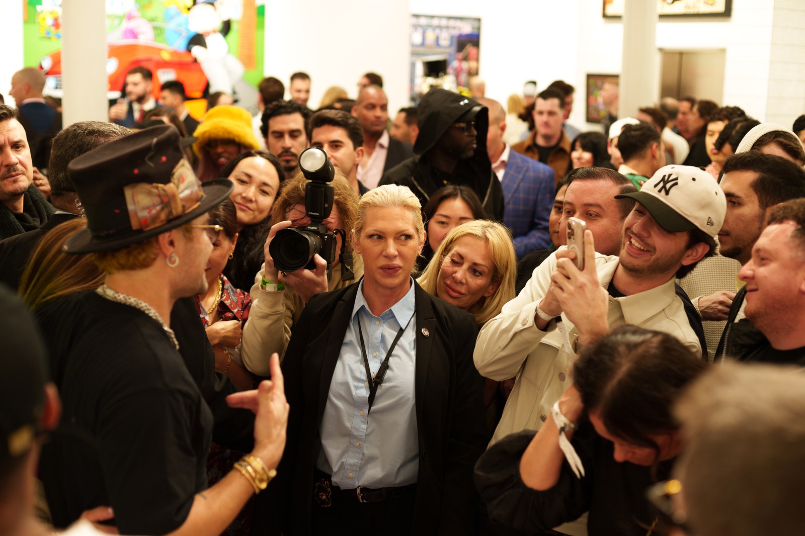 A photographer with a camera stands among a dense crowd of guests, several raising phones to film