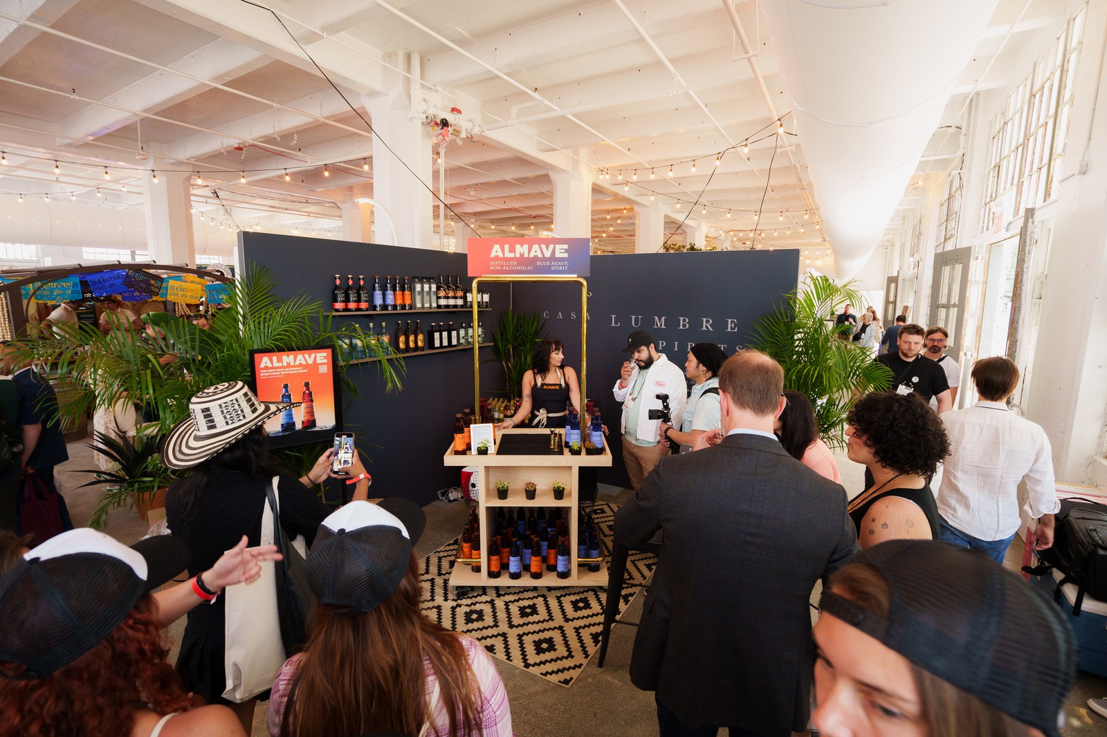 Almave bar stand with a dark backdrop, potted palms and a patterned rug inside a white columned hall