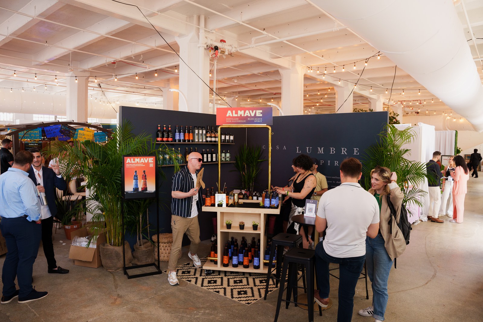 Guests gather at the Almave booth under string lights in a bright white columned hall
