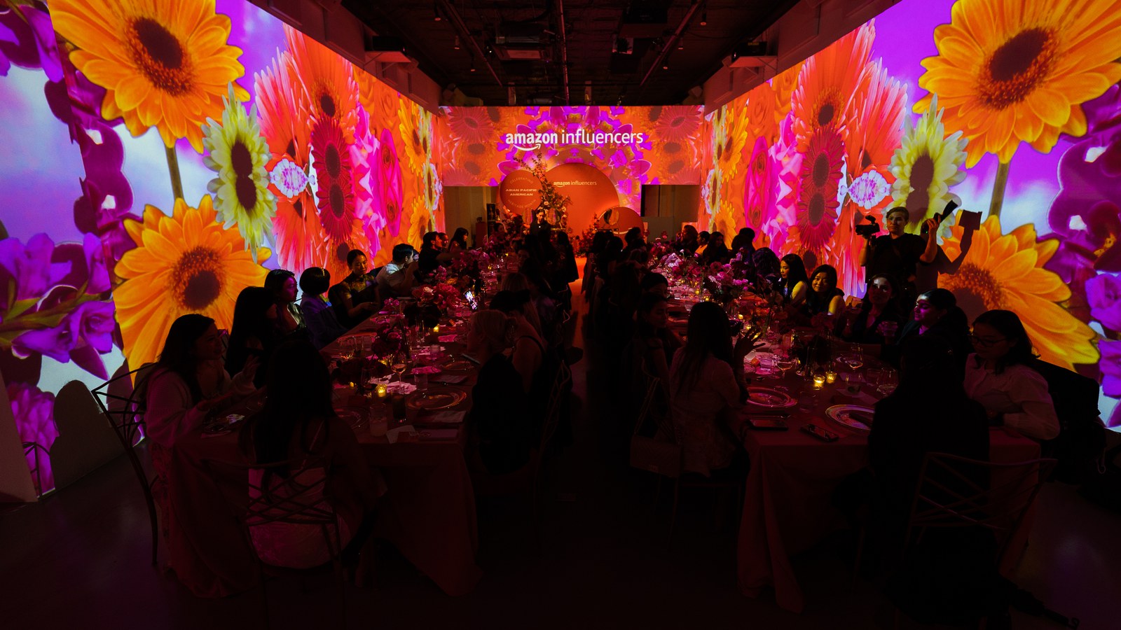 Server carries green cocktails on a tray scattered with rose petals under pink light