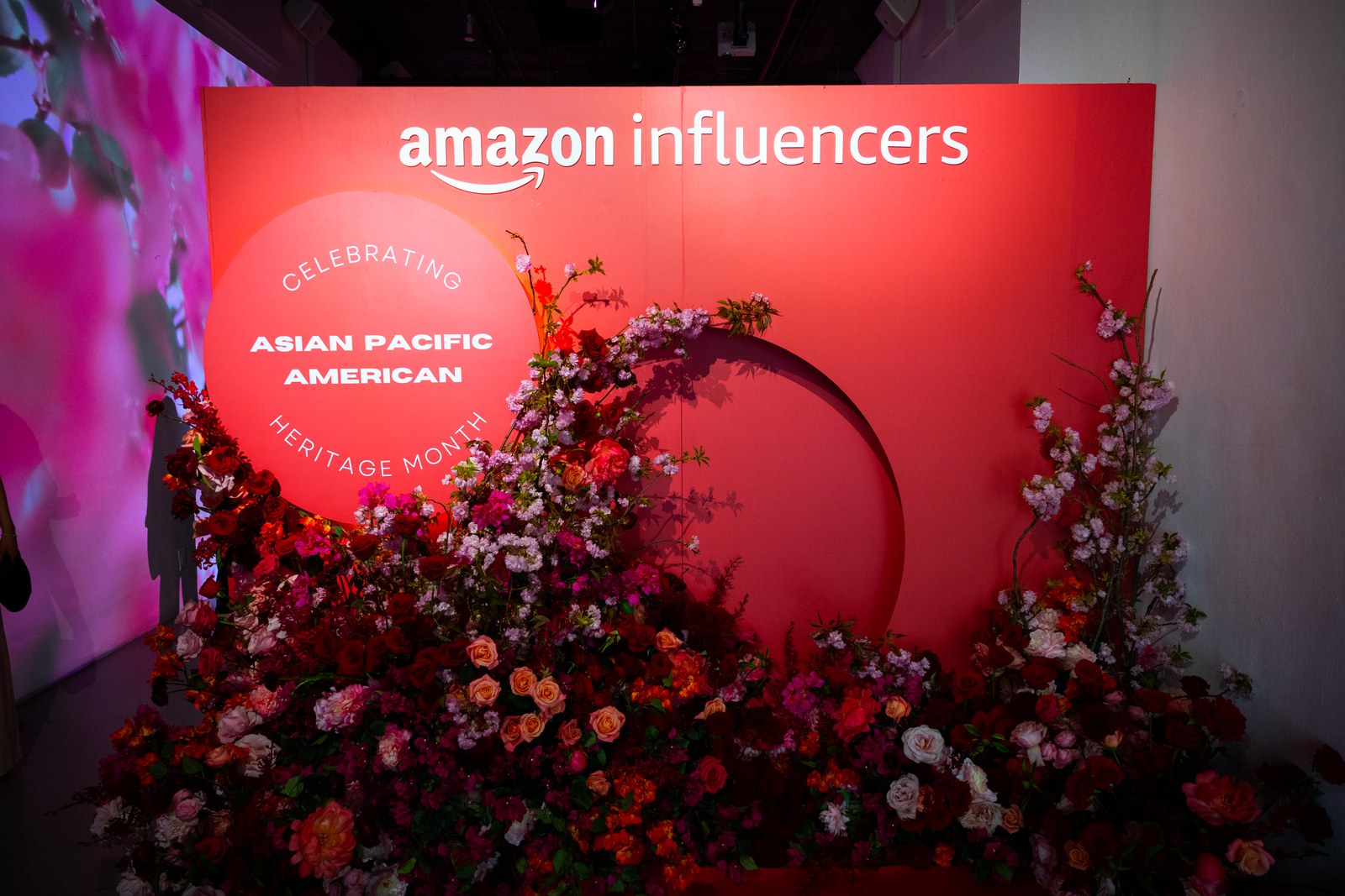 Three guests chat with drinks beneath a blossom projection at the Amazon Influencers dinner
