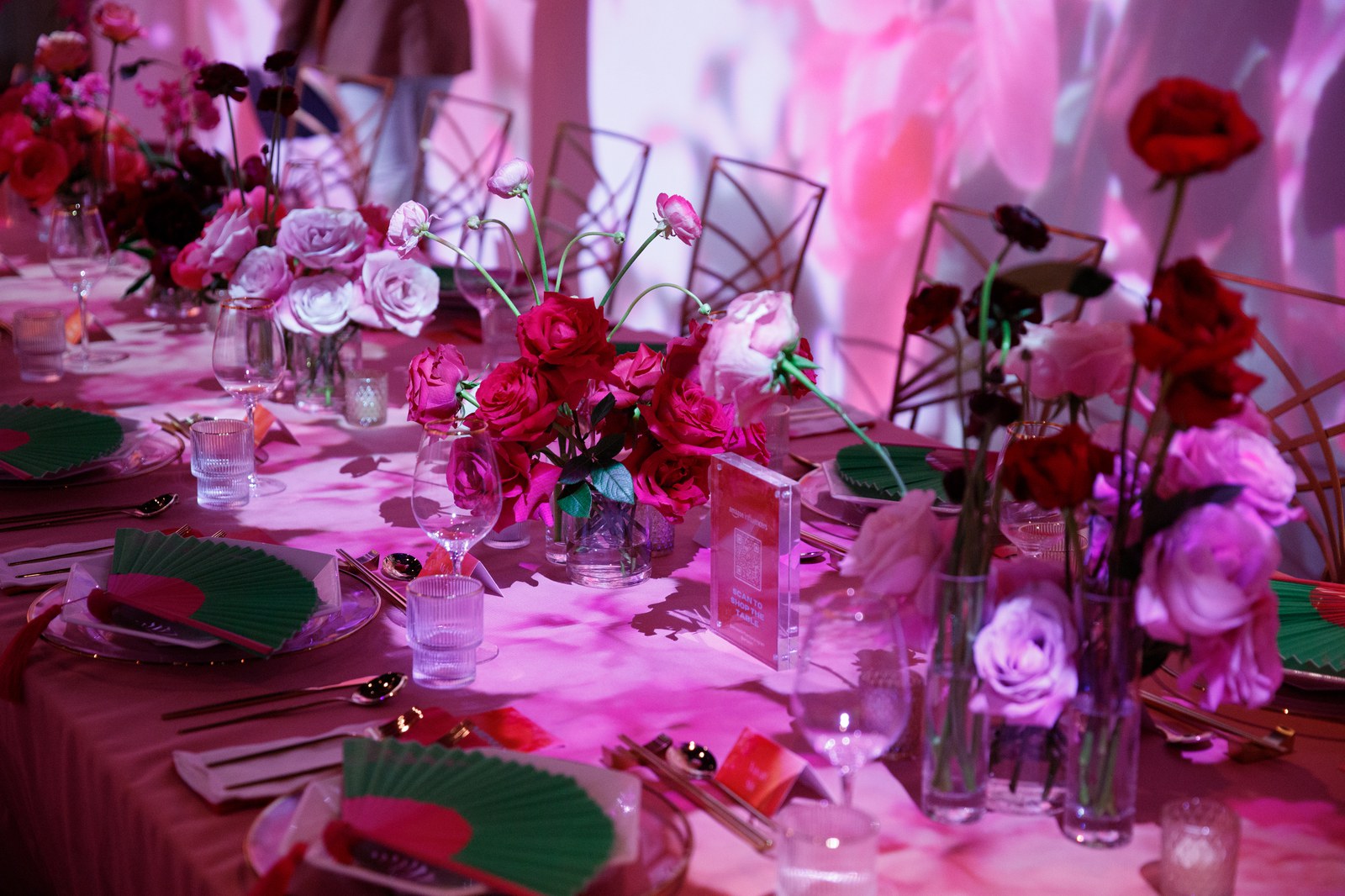 Long dinner table with red and pink roses, gold chairs and projected pink light on the walls