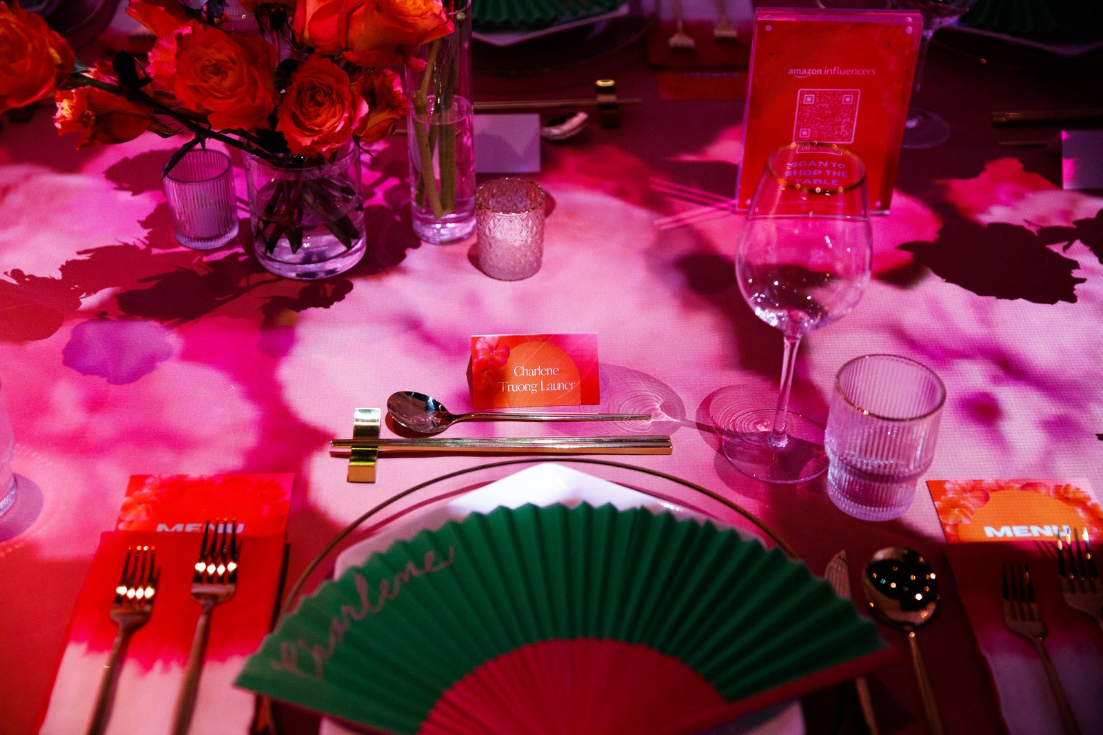 Table set in pink and red light with orange roses, a green and red paper fan and gold cutlery