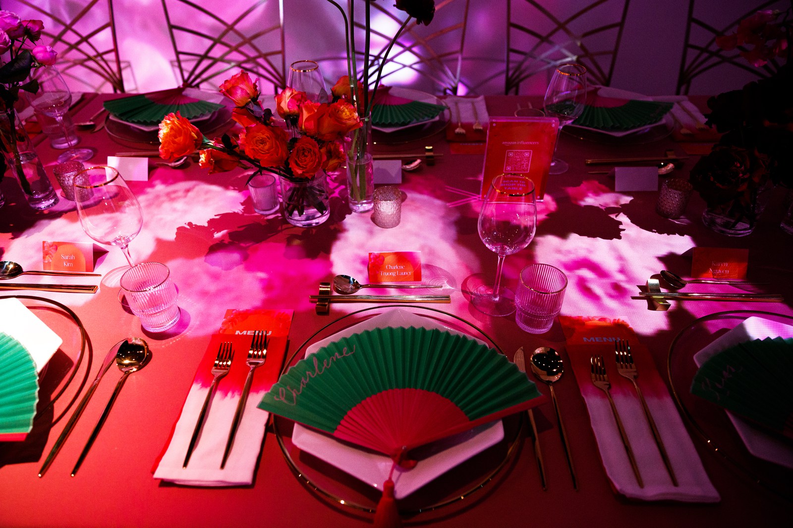 Red and green folding fans on white napkins at a table lit by pink and white projections