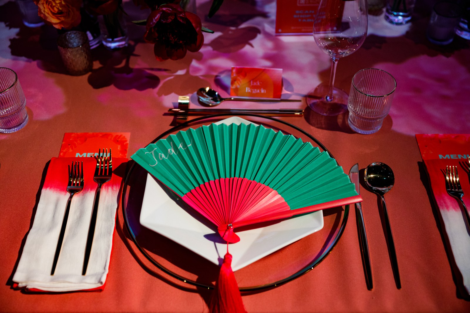 A green and red folding fan with a red tassel rests on a plate between gold cutlery