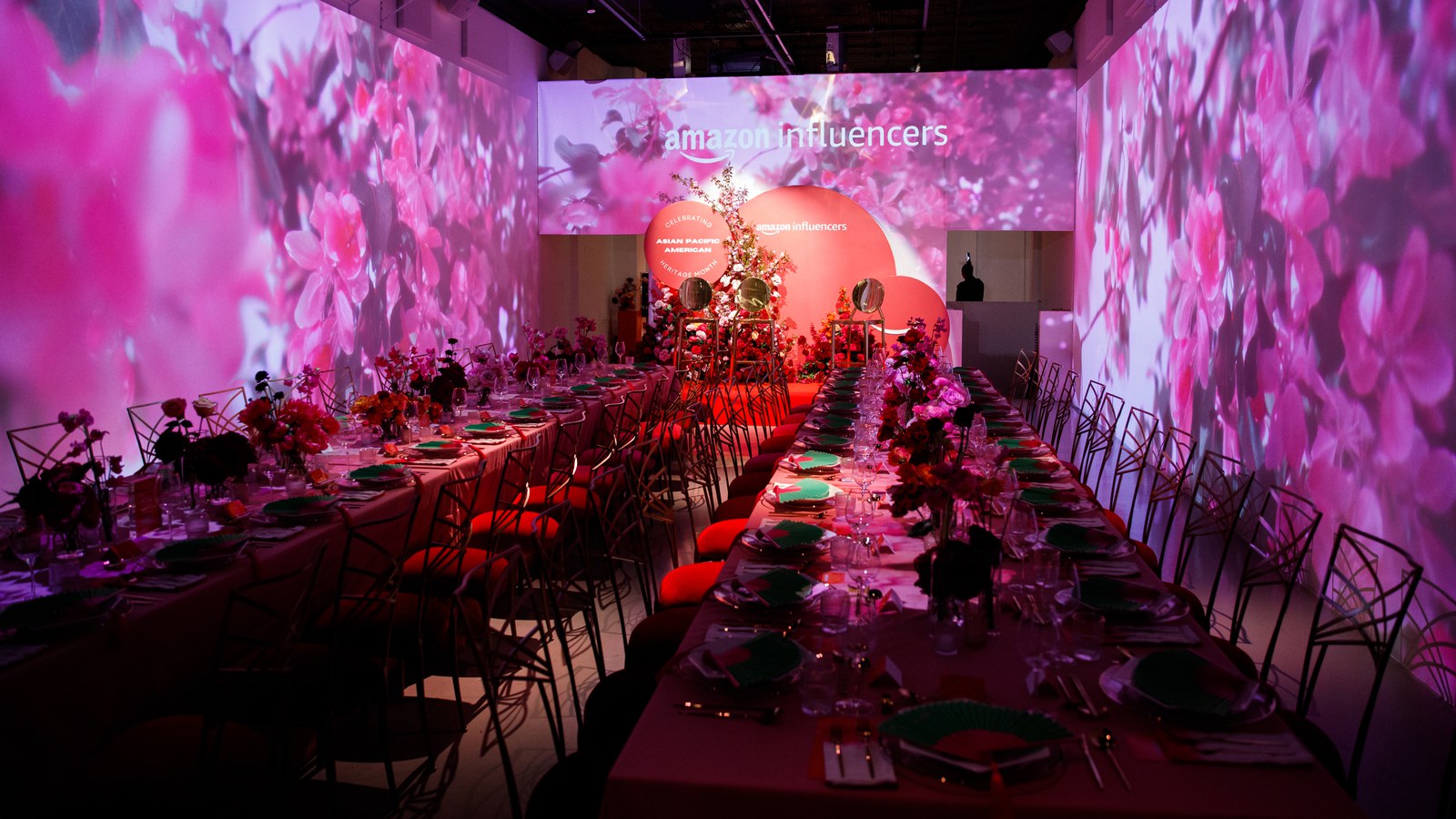 Long banquet tables with green plates fill a room where blossoms and Amazon Influencers are projected on the walls