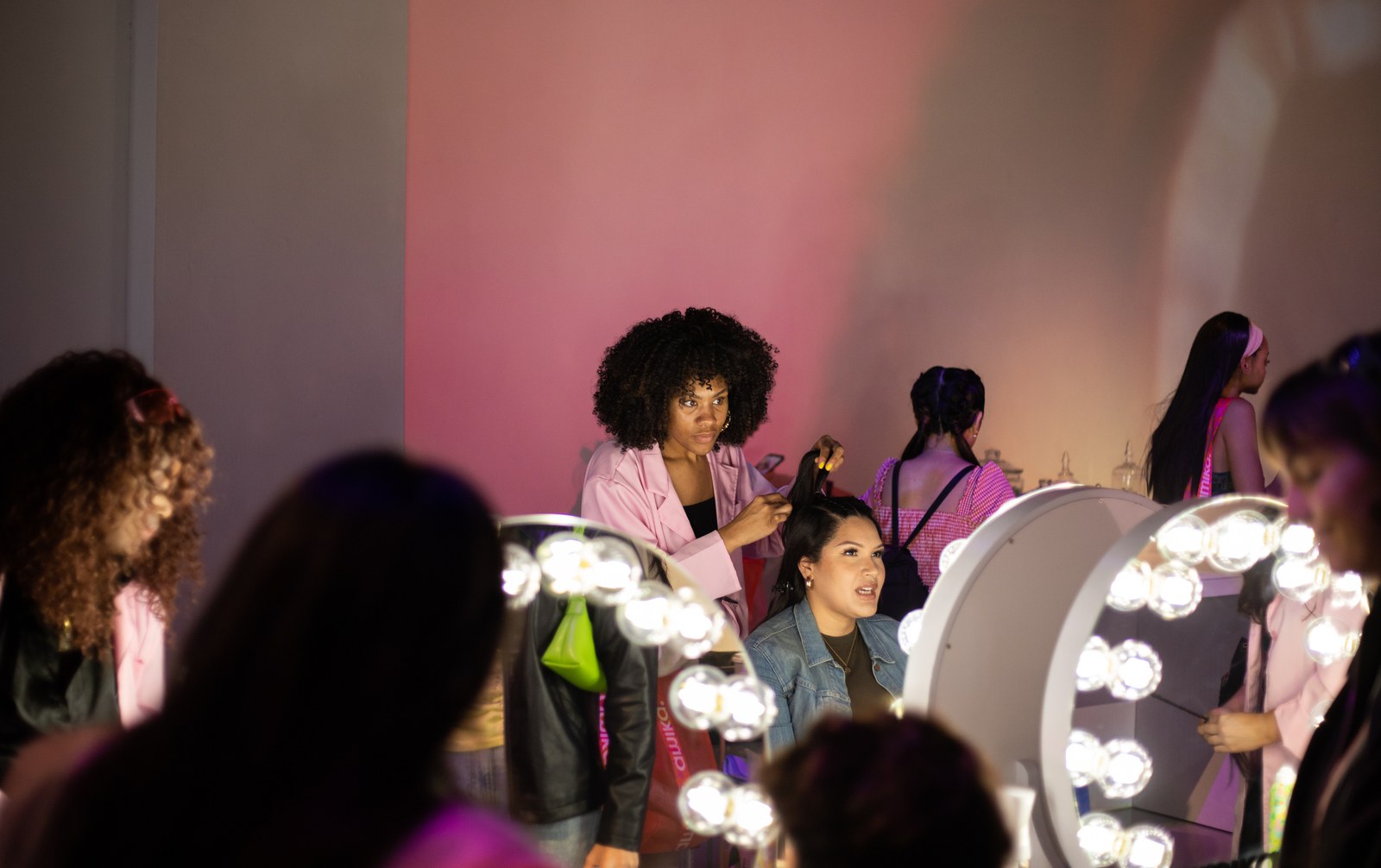Stylists in pink jackets work on seated guests at round lighted mirrors for Amika at Lume Studios in Tribeca, Manhattan.