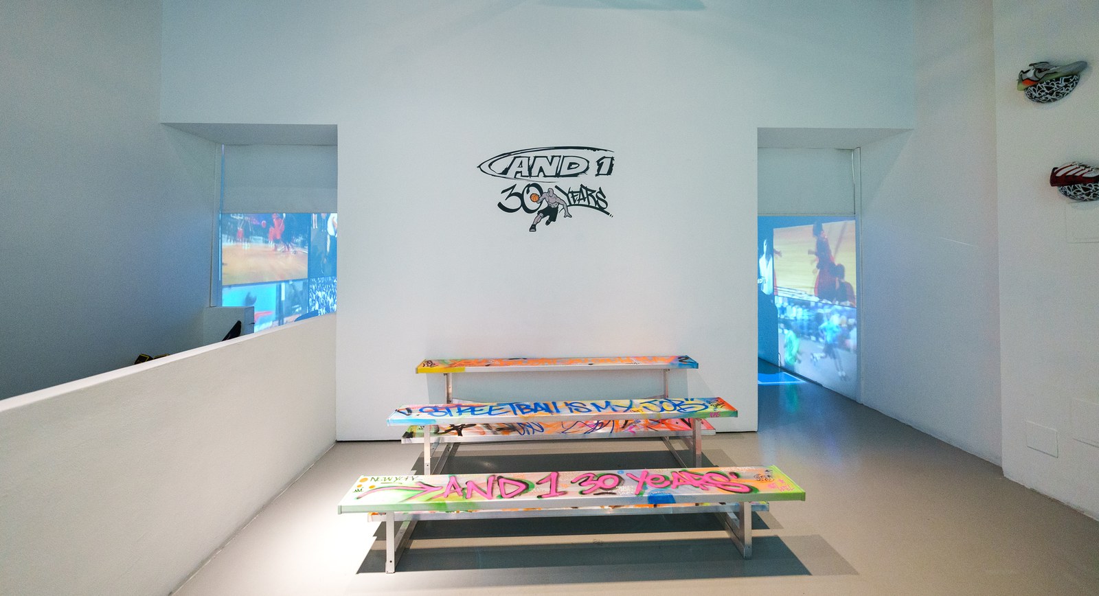 Two graffiti painted benches below an AND1 30 Years logo on a white gallery wall with projected screens either side