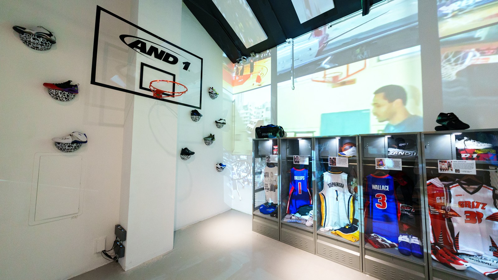 White room with an AND1 backboard on the wall, sneakers mounted on shelves and glass lockers holding basketball jerseys